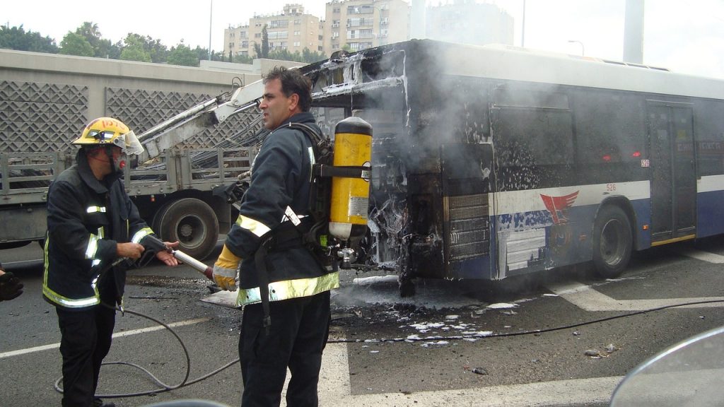 An image showcasing a firefighter in full gear, standing in front of a partially burnt building